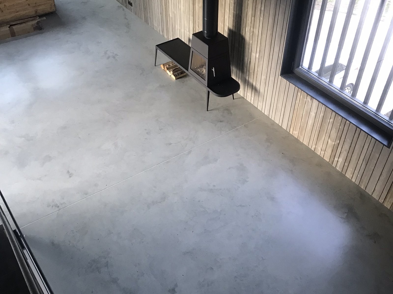 Sichtestrich in Hellgrau in einem Loft mit Pelletofen und Holzwand – moderne Wohnatmosphäre